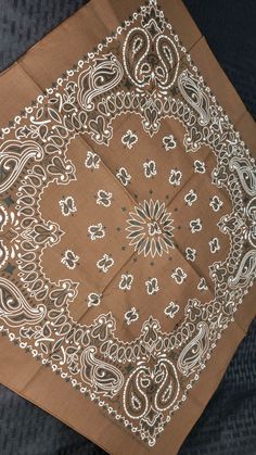 a brown and white bandanna on top of a black cloth with an intricate design