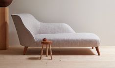 a white chaise lounge chair sitting in front of a clock on a wooden stand