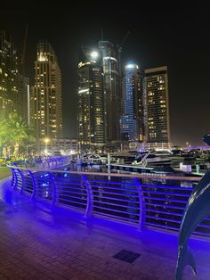 the city skyline is lit up at night with blue lights in the foreground and boats on the water