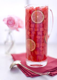 a pitcher filled with liquid sitting on top of a red cloth next to a spoon