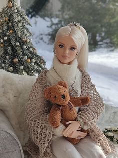 a doll sitting on a couch holding a teddy bear in front of a christmas tree