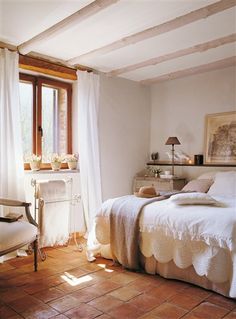 a bed sitting in a bedroom under a window next to a chair and table with flowers on it