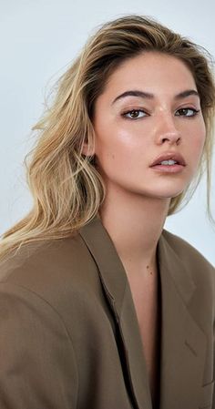 a woman with long blonde hair wearing a brown blazer and looking off to the side