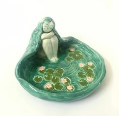 a ceramic figurine sitting on top of a green bowl filled with water lilies