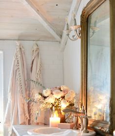 a bathroom sink sitting under a mirror next to a vase with flowers on top of it