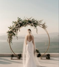 a bride standing in front of an arch with flowers and greenery on top of it