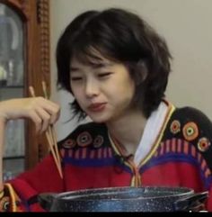 a woman sitting at a table with scissors in her hand and looking down at the bowl