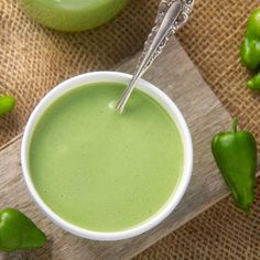 a cup filled with green liquid sitting on top of a wooden table next to peppers