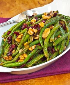 green beans with cranberries and walnuts in a white bowl on a purple placemat