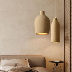 two lamps hanging from the ceiling above a bed in a room with beige walls and pillows