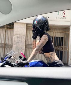 a tattooed man riding on the back of a motorcycle next to a gated building