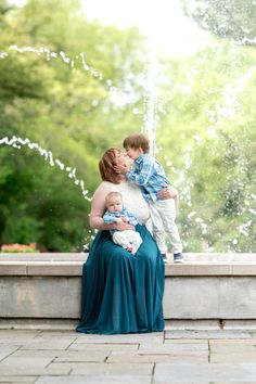 a mother and her son are sitting on a fountain with water shooting up in the air