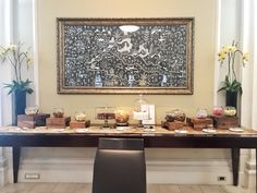 a long table is covered with desserts and candles in front of a painting on the wall