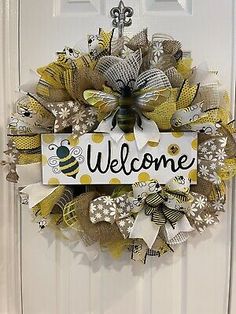 a yellow and white welcome wreath hanging on a door with the word welcome written on it