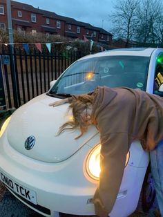 a woman leaning on the hood of a white car with her head in the window