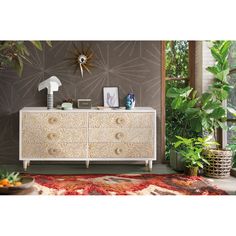 a white dresser sitting in front of a window next to a potted plant on top of a rug