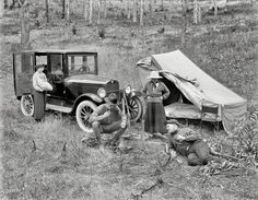 an old black and white photo of men working on a car with a tent in the background