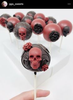 a hand holding a skewer filled with red and black cake pops covered in skulls