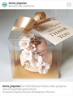 a cake in a clear box with a gold ribbon and flowers on the top that says thank you