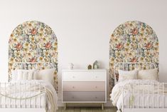 two white beds with floral wallpaper in a bedroom