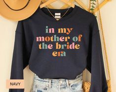 a sweater that says in my mother of the bride era on it next to a straw hat