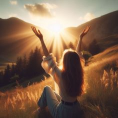 a woman is sitting in the grass with her arms up and hands raised above her head