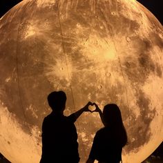 two people standing next to each other in front of a large moon with the shape of a heart