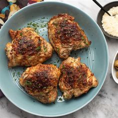 four pieces of chicken on a blue plate with olives and mashed potatoes next to it