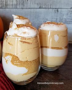 two glasses filled with dessert sitting on top of a table next to an orange pumpkin