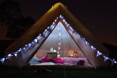 a tent that has lights on it in the grass at night with pillows and blankets