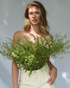 a woman holding a bouquet of flowers in front of her face and looking at the camera