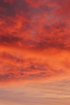 an airplane is flying in the sky with red and orange clouds behind it at sunset