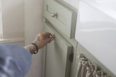 a person with tattoos on their arm is opening the door to a white cabinet in a bathroom