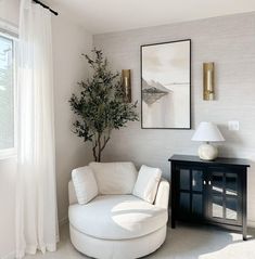 a living room with white furniture and a tree in the corner on the side table