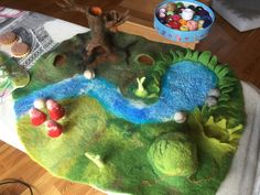 a table topped with a green rug covered in animals and trees next to a bowl of candy