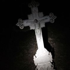 a cross lit up in the dark with light shining on it's face and arms