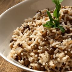 a white bowl filled with rice and beans on top of a wooden table next to a green leaf