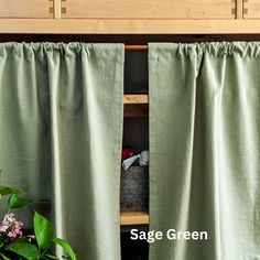 green curtains are open in front of a wooden shelf with plants and other items on it