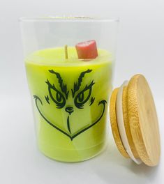 a yellow candle with an angry face on it next to a wooden lid