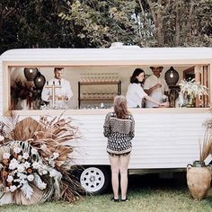 a woman standing in front of a food truck with flowers and plants on the side