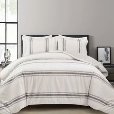 a white bed with black and grey striped comforter set on top of it in front of a window