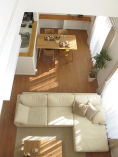 an overhead view of a living room and dining room with hardwood floors, white couches, coffee table and open kitchen area