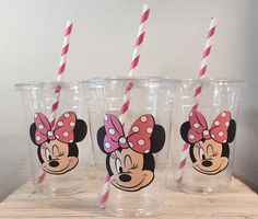 three minnie mouse cups with pink and white straws in them on a wooden table