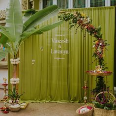 a green backdrop with flowers and greenery on the side, along with other decorations