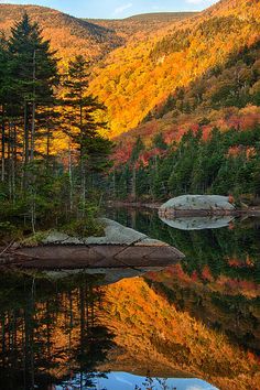 the mountains are covered in autumn foliage and trees with their leaves changing colors as they reflect in the still water