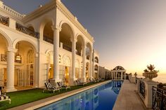 an outdoor swimming pool in front of a large white building with columns and arches on the sides