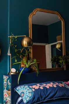 a bedroom with blue walls and plants on the nightstand next to the bed in front of the mirror