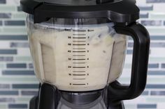 a blender filled with white liquid sitting on top of a counter next to a tiled wall