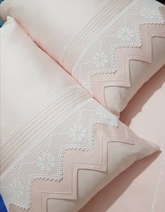 two pillows with white lace on them sitting next to each other