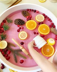 a bowl filled with oranges, cranberries and pine cones on top of a table